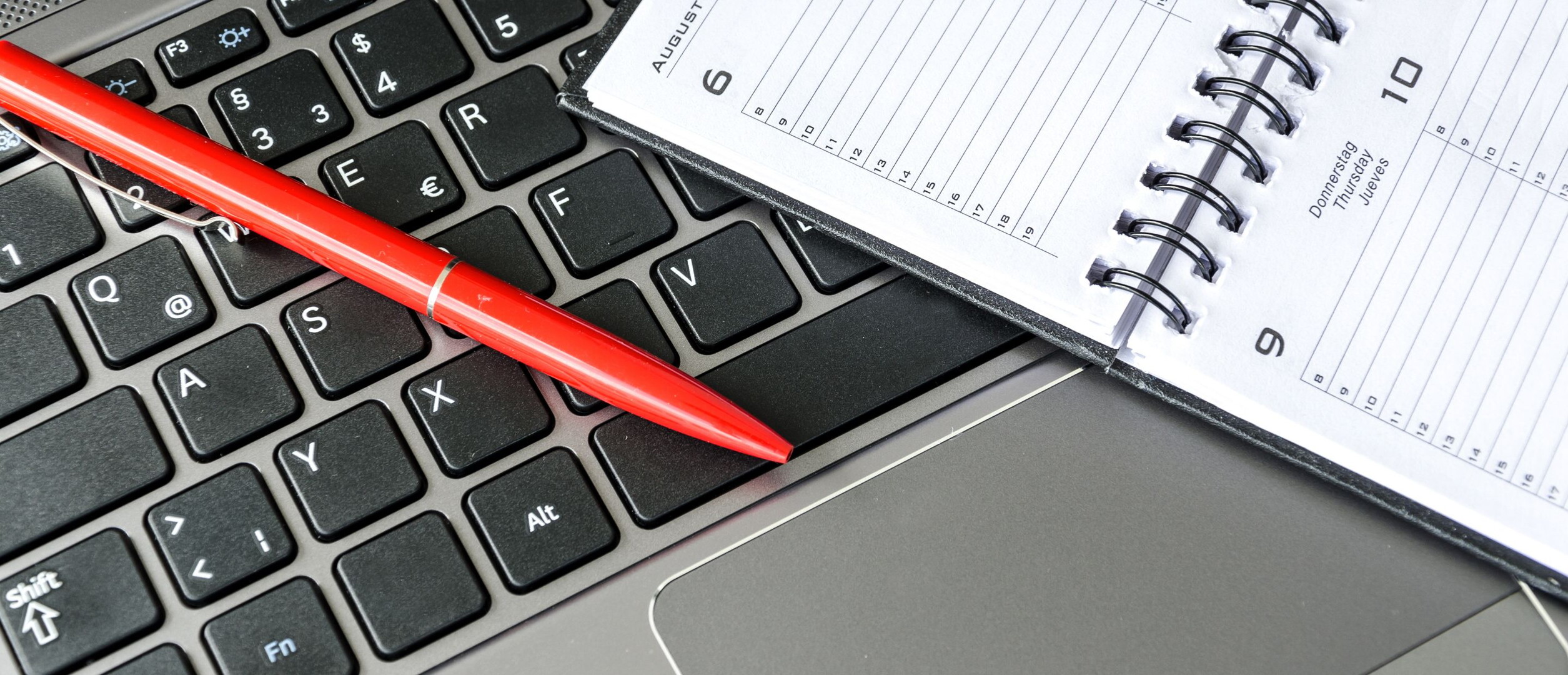 Roter Stift und aufgeschlagener Terminkalender auf einer Laptop-Tastatur