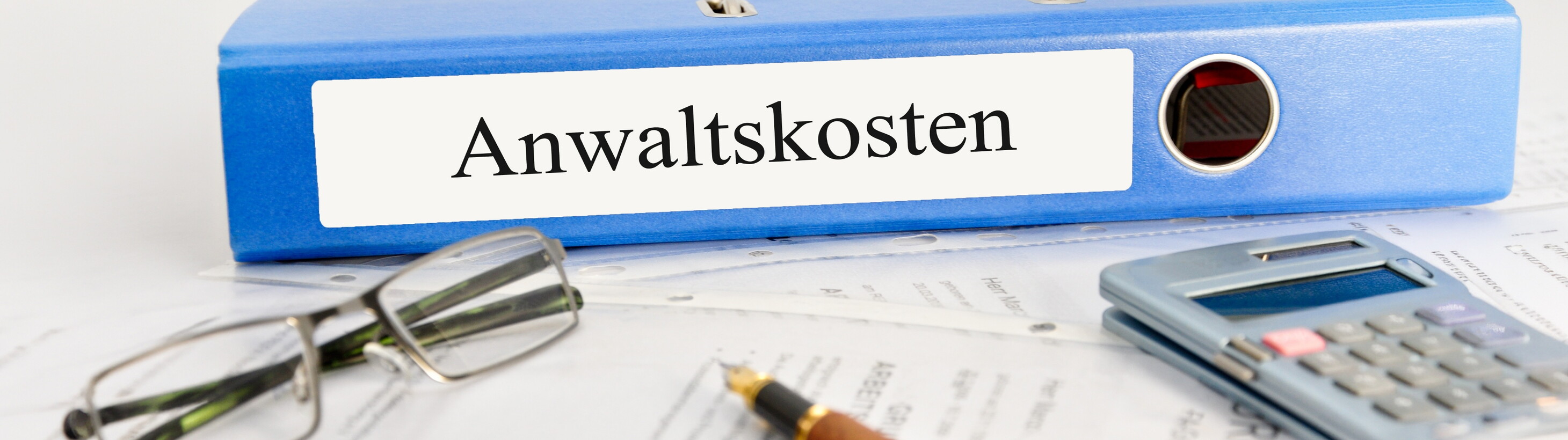 Aktenordner mit der Aufschrift „Anwaltskosten“, daneben Brille, Taschenrechner und Unterlagen